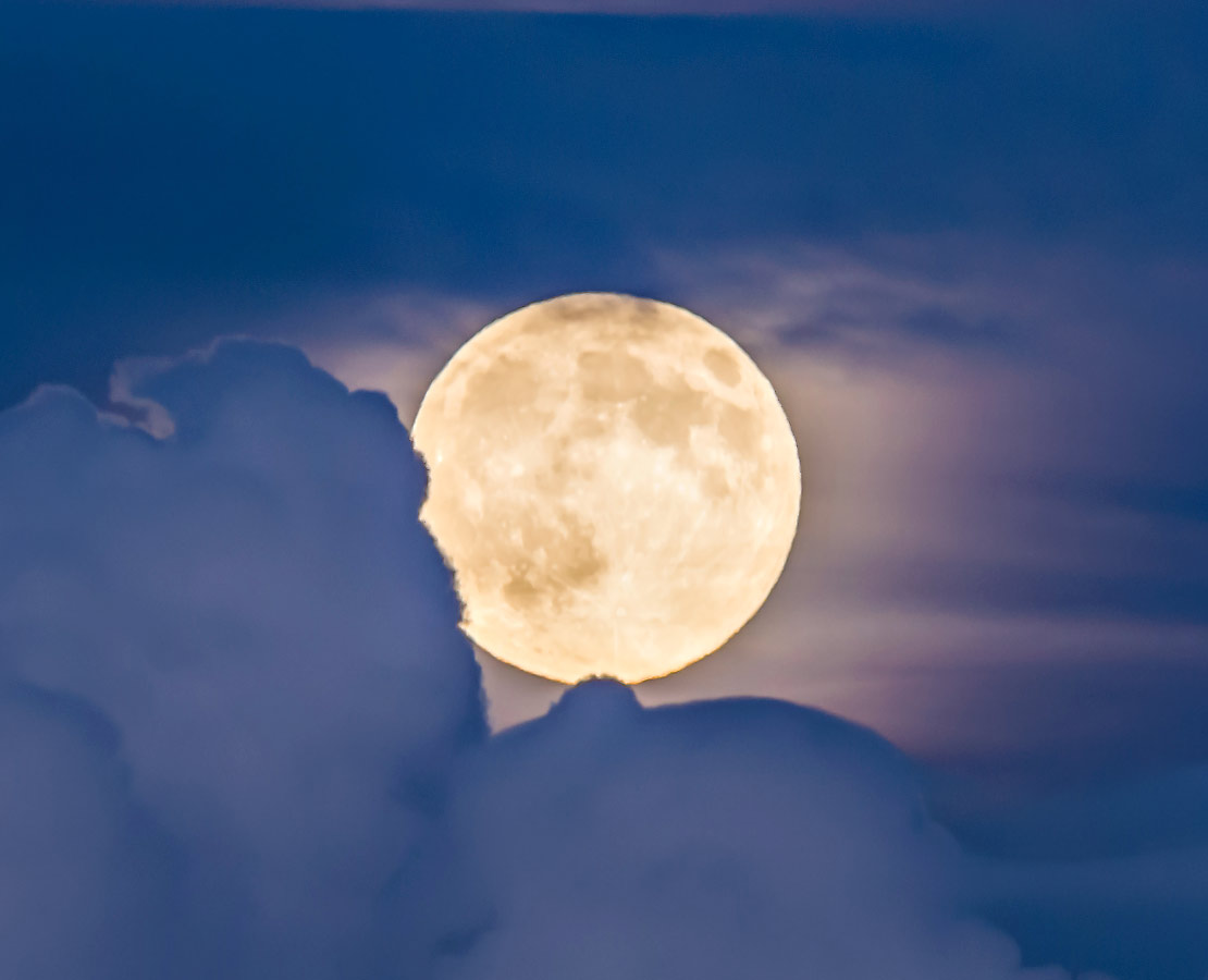 La pleine lune se lève derrière des nuages au crépuscule...